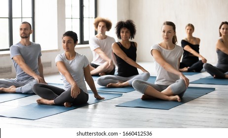 Horizontal image seven multi-ethnic people during yoga class seated in lotus position performing Easy Twist Pose or Parivrtta Sukhasana. Exercise decrease feeling of nervousness, reduce stress concept - Powered by Shutterstock