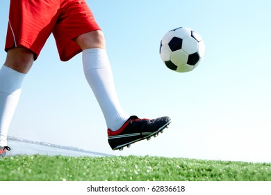 Horizontal image of soccer ball being kicked by footballer against blue sky