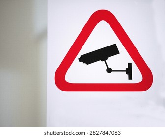 Horizontal image of surveillance camera warning sign with red triangle on light background, highlighting security monitoring and safety awareness concept.