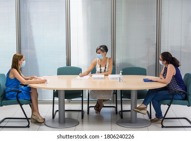 Horizontal Image Of Three Women In A Meeting Room With Masks Maintaining Social Distance Due To Covid-19 In A Work Meeting