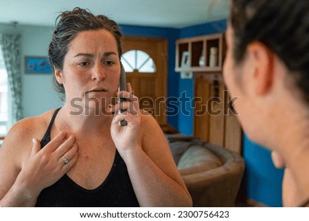 Horizontal image of young female in mirror reflection calling doctor about concerns of skin cancer on chest.