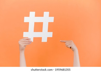 Horizontal images of female hands holding and pointing on large big hashtag sign, viral web content, internet promotion, isolated on pastel orange studio wall. Blogging blog website strategy concept