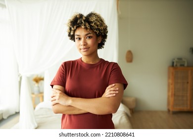 Horizontal Indoor Portrait Of African American Woman Standing In Bedroom With Confident Smile Looking At Camera With Folded Arms, Wearing Red T-shirt. Happy Real Estate Owner. Daily Life