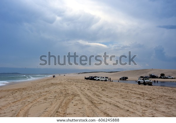Horizontal landscape of the beach with\
cars. 4wd cars at Crokers creek (Belmont - Nine Miles - Beach, NSW,\
Australia). Redhead Point in the\
background.