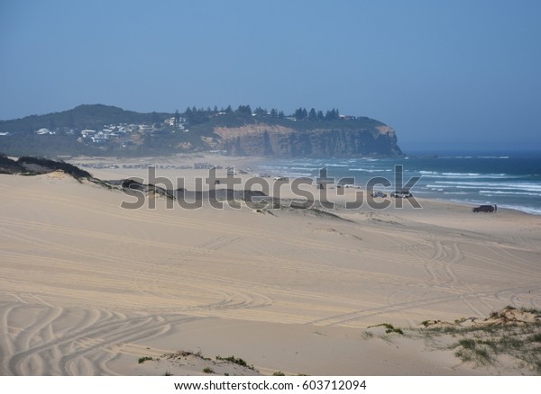 Horizontal landscape of\
the beach with sand dunes and cars (Belmont - Nine Miles - Beach,\
NSW, Australia)