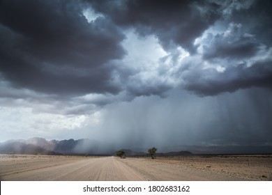 A Horizontal Landscape Photograph Of A Road Leading To A Massive Dramatic Rain And Thunder Storm With Mountains In The Distance In The Dry Namib Desert Near Sesriem And Sossusvlei.