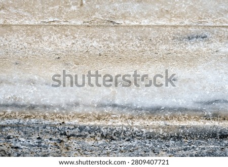 Horizontal layers of weathered stone display rough crystalline surfaces. A dark gray base supports lighter, porous mineral deposits with visible striations and granular texture