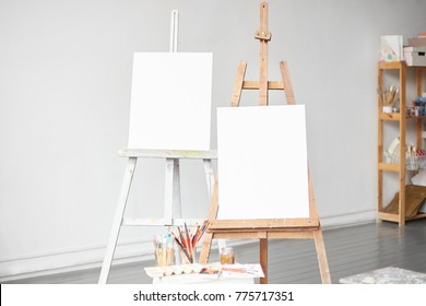 Horizontal light shot of painter workplace mock up. Watercolor, brushes and accessories. Two wooden easels with blank painting canvas as copy space for mock up isolated on artistic studio background.