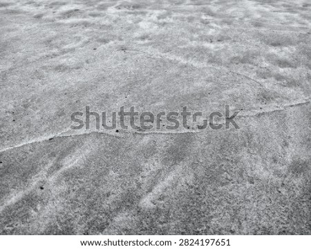 Horizontal low angle perspective of wet grey beach sand texture with curved sea wave water lines and subtle tide marks.