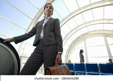 Horizontal Low Angle Shot Of A Businesswoman Standing Besides An Escalator In Airport Departure Lounge Looks At The Camera.