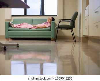 Horizontal Low Angle Shot Of A Nurse Lying On A Sofa During Break Time In A Hospital Staff Room.