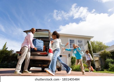 Horizontal low angle shot of two playful children running by the father packing a suitcase into a car with mother striding in the background. - Powered by Shutterstock