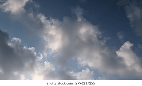 Horizontal low-angle shot of a dramatic blue sky filled with fluffy cumulus clouds, highlighting the beautiful contrast between bright white sunlit edges and soft gray shadows in the morning.