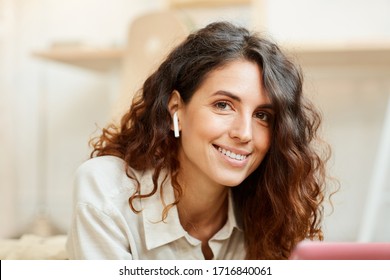 Horizontal medium close-up portrait of young adult woman with beautiful curly hair looking at camera smiling