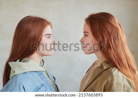 Horizontal medium close-up side view portrait of young female twins standing in front of each other, looking at each other