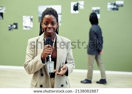 Horizontal medium portrait of young African American art gallery curator holding microphone speaking about current exhibition