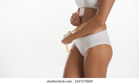 Horizontal medium shot of African American fit good-looking woman in underwear measures her waistline using tape on white background | Body health care concept