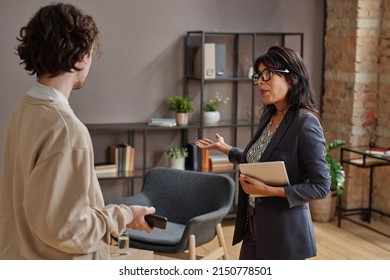 Horizontal medium shot of modern professional psychologist inviting young man and offering him to take seat - Shutterstock ID 2150778501