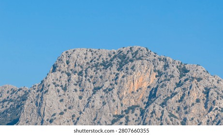 Horizontal medium shot of textured limestone mountain peaks under a blue sky with fluffy white clouds in Antalya