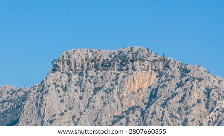 Horizontal medium shot of textured limestone mountain peaks under a blue sky with fluffy white clouds in Antalya