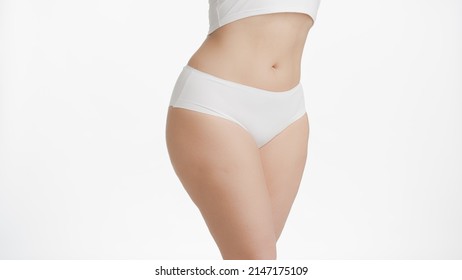 Horizontal medium shot of white-skinned plus size woman's waist and hips in white underwear on white background | Body care concept