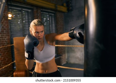 Horizontal Medium Shot Of Young Woman With Hands In Boxing Gloves Punching Heavy Bag