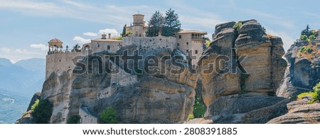 Horizontal panoramic eye level shot of the historic varlaam monastery complex built on a giant sandstone cliff rock formation in meteora greece on a sunny day.