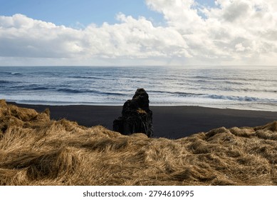 Horizontal panoramic view from a cliff overlooking Reynisfjara black sand beach with an isolated basalt rock formation, Iceland