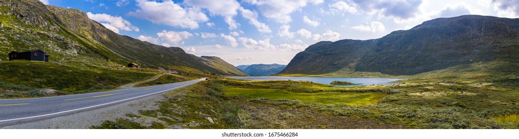 Horizontal Panoramic View Of Winding Road Along Mountains And Lake. Breathtaking Mountain Landscape Of The Norwegian Nature. Ultimate Road Trip Destination To Scandinavia. Green Moss Clouds Blue Sky. 