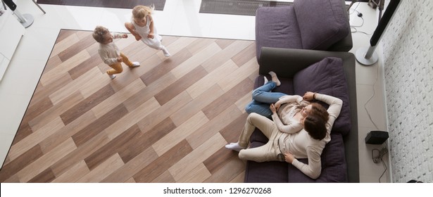 Horizontal Photo Above View Couple Resting Sitting On Couch, Small Kids Play Run In Living Room At New Home, Relocation And Buy House Concept, Banner For Website Header Design With Copy Space For Text