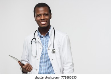 Horizontal photo of african doctor isolated on grey background smiling happily and holding his tablet computer. Concept of contemporary gadgets and medical services 