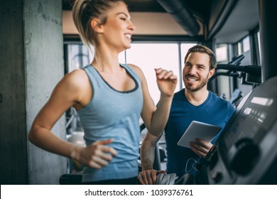 Horizontal Photo Of Attractive Woman Jogging On Treadmill At Health Club. Training With Fitness Instructor.