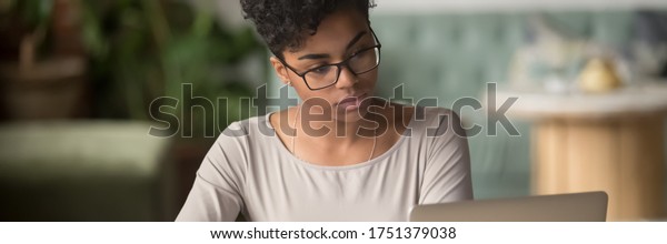 Horizontal photo banner for website header\
design, African student girl wear glasses sit indoors look at pc\
screen study on-line, do assignment, prepare for university\
admission exams, e-study\
concept