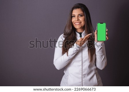 Horizontal photo. brazilian woman with medical coat, nutritionist. holding smartphone, green screen. slimming.