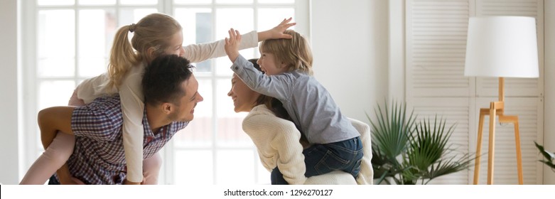 Horizontal Photo Cheerful Parents Laughing Piggybacking Little Kids Play In Living Room At Home Family Having Fun Enjoy Time Together Concept, Banner For Website Header Design With Copy Space For Text