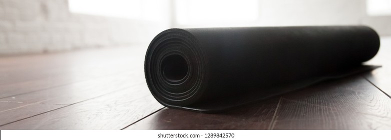 Horizontal photo close up black yoga fitness floor mat in a roll inside of gym studio. Active lifestyle healthy habit sport fitness concept. Banner for website header design with copyspace for text