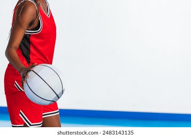 Horizontal photo close-up of a female basketball player in a red uniform dribbling a basketball on an indoor court, highlighting her focus and control during practice or a game. Sport concept. - Powered by Shutterstock