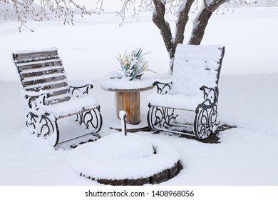 A Horizontal Photo Of A Couple Rocking Chairs Covered With Snow At The Fire Pit.