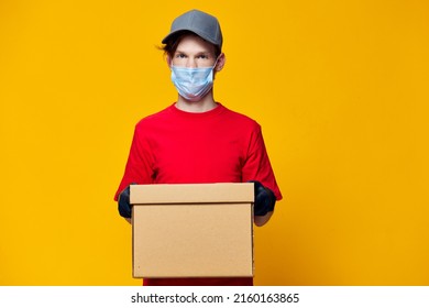 horizontal photo of a courier in a mask with a cardboard box in his hands - Shutterstock ID 2160163865