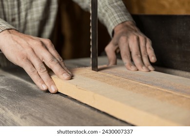 Horizontal photo a focused shot capturing a carpenter's hands as they guide a piece of timber with blue markings along the steady path of a bandsaw blade. Business concept. - Powered by Shutterstock