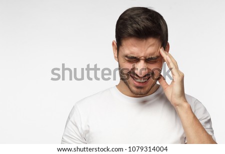 Horizontal photo of good-looking Caucasian man pictured isolated on gray background in right side of picture showing how much his head hurts, experiencing pain, looking miserable and exhausted