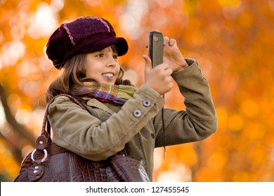 horizontal photo, happy beautiful little girl take a photograph on  mobile phone, autumnal portrait - Shutterstock ID 127455545