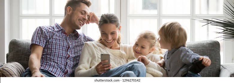 Horizontal photo happy family with little kids watching funny video on phone sitting on couch enjoy weekend at home, modern tech leisure activities free time concept, banner for website header design - Powered by Shutterstock