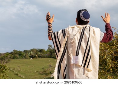 Horizontal photo of Juido Latino wearing tefilin and kippah raising his hands praying while looking at the sky with a beautiful background of natuleza. - Shutterstock ID 2096109658