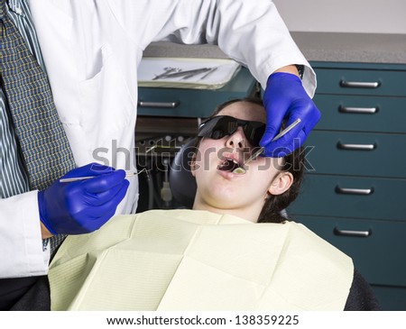 Horizontal photo of a male dentist preparing to examine young girl teeth with tools in tray in background