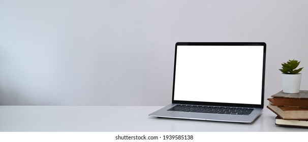 Horizontal photo of minimal workplace with computer laptop, plant and book on white desk.