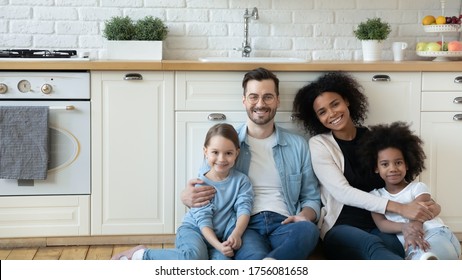 Horizontal Photo Multiracial Excited Couple With Adorable Daughters Sit In Modern Renovated Kitchen On Warm Floor Smile Look At Camera. New Property Owners, Happy Multicultural Family Portrait Concept