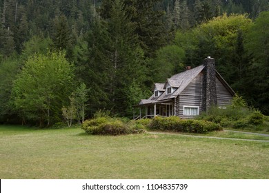 Horizontal photo of an Old Mountainside Log Cabin surrounded by trees, shrubs and grass