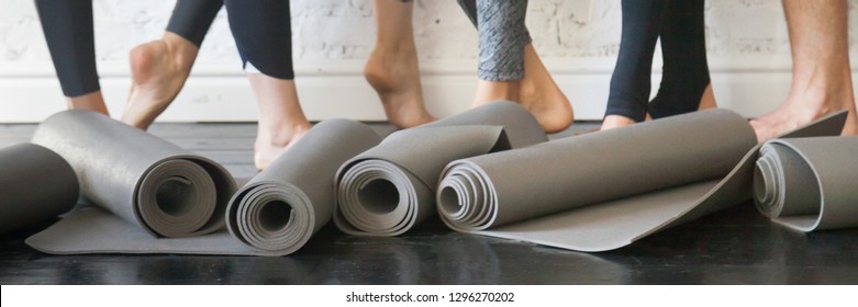Horizontal photo people standing after work out, close up yoga mats grey carpets in roll and athlete barefoot legs. Group training, active lifestyle in club concept. Banner for website header design
