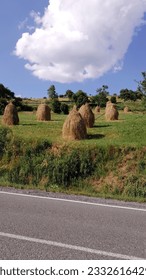 Horizontal photo of sheaves of hay on a green hill by the road - Shutterstock ID 2332616429